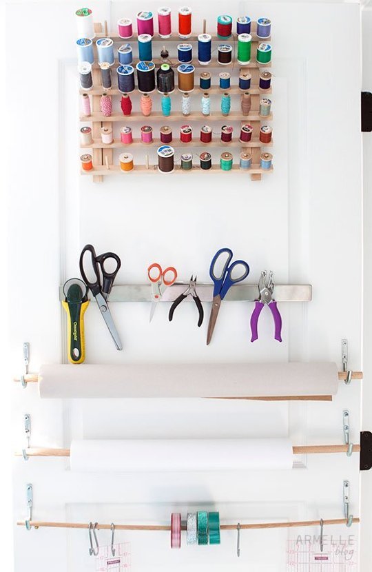 Organized craft room door with thread storage rack, paper dispensers, and a magnetized tool holder. 