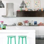 a modern kitchen with colorful design details like art, books on a shelf and mint green glossy painted stools